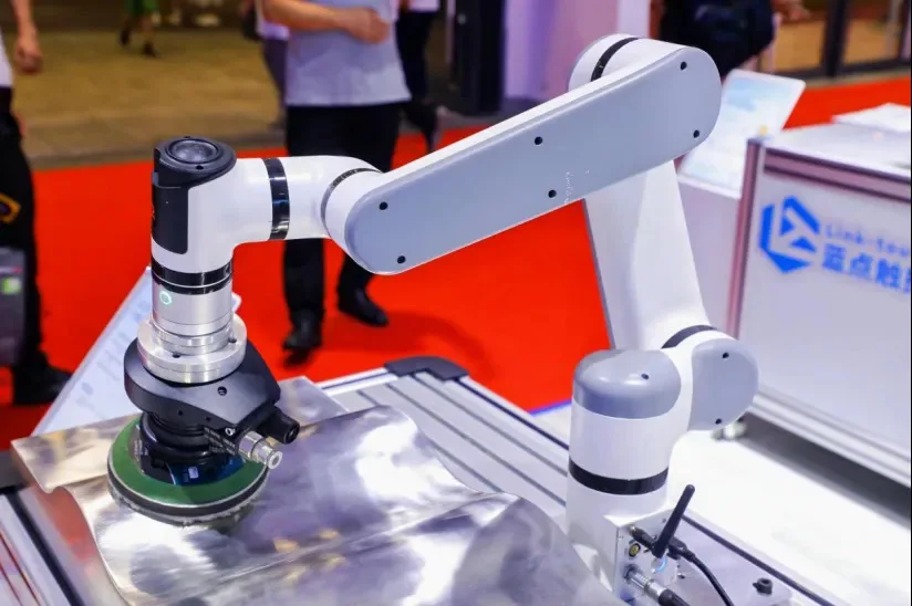 Collaborative robot arm (cobot) carefully polishing a curved metal part in an industrial manufacturing setting.