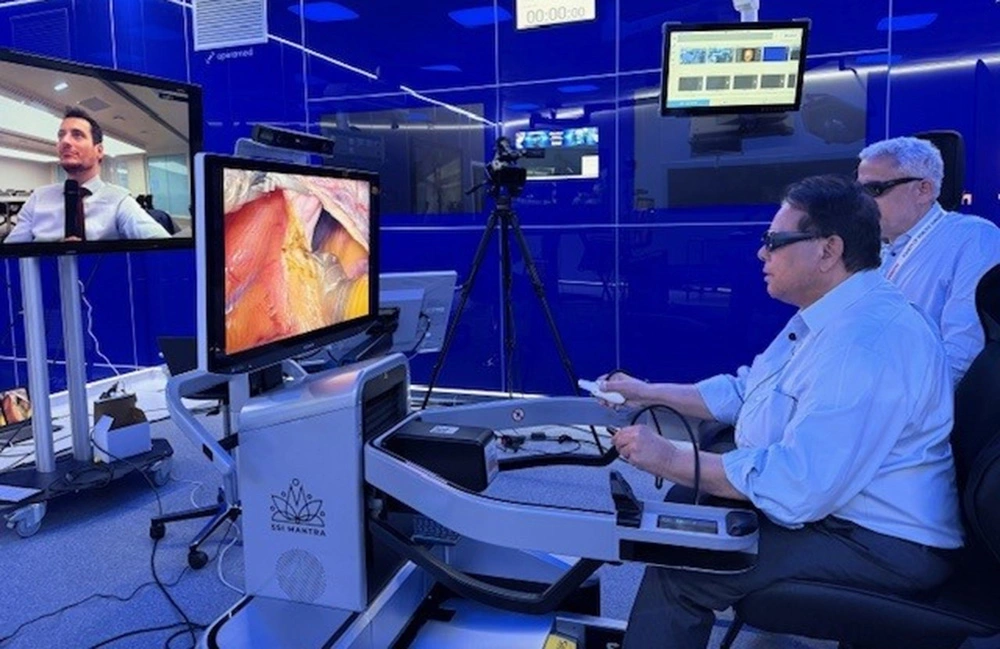 A surgeon at a console performs remote robotic surgery, using joysticks to control instruments while viewing a screen