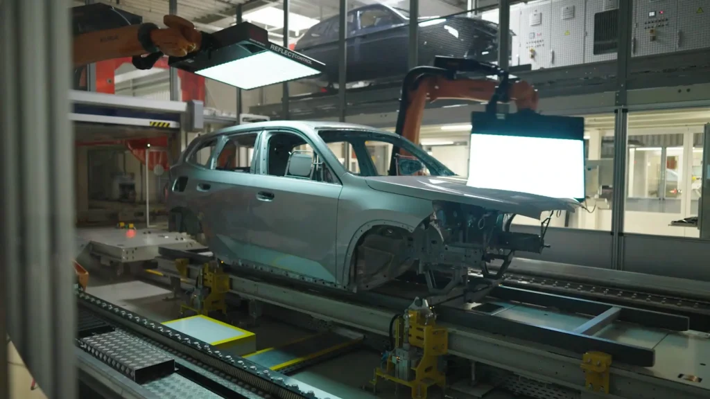 Robotic arms with lights performing an automated visual inspection of a car body on a manufacturing assembly line for quality control