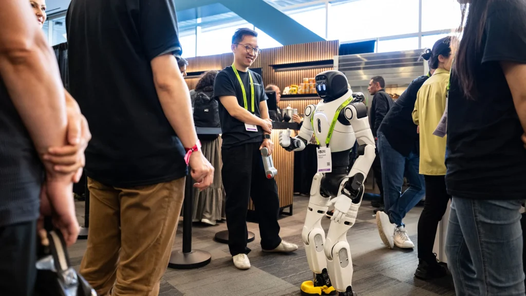 A friendly humanoid robot with yellow shoes interacting with attendees at a tech conference, demonstrating human-robot interaction
