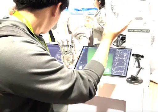 A person uses motion capture to control a robotic hand, which mimics their movements in real-time at a technology demo
