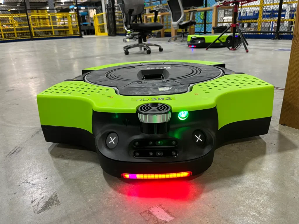 Close-up of a bright green autonomous mobile robot (AMR) on a warehouse floor, showing its sensors and status lights