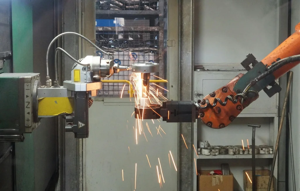 An industrial robotic arm in a factory performs a grinding operation on a metal part, creating a shower of bright sparks
