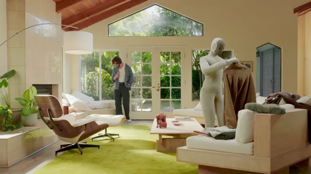 A sleek humanoid robot folds clothes in a sunlit living room, demonstrating the future of AI-powered home assistance