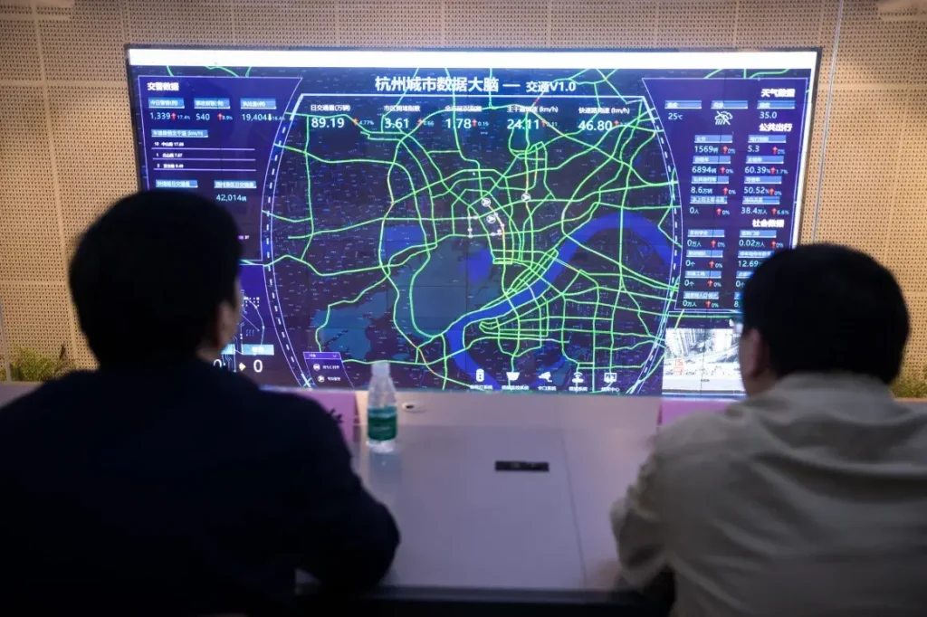 Two people in a control center monitoring a large screen that displays a city's real-time traffic data map