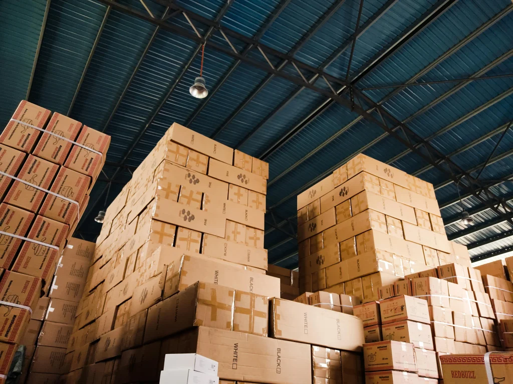 Upward shot of a warehouse ceiling with tall stacks of cardboard boxes, representing inventory and supply chain management