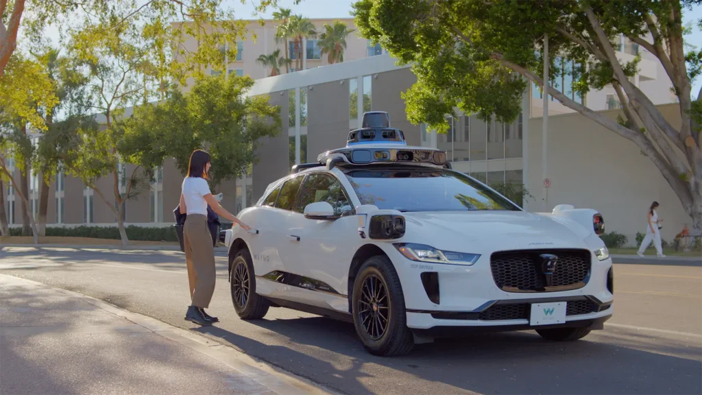 A woman getting into a white Waymo self-driving car, a Jaguar I-PACE equipped with Lidar and camera sensors, for a ride