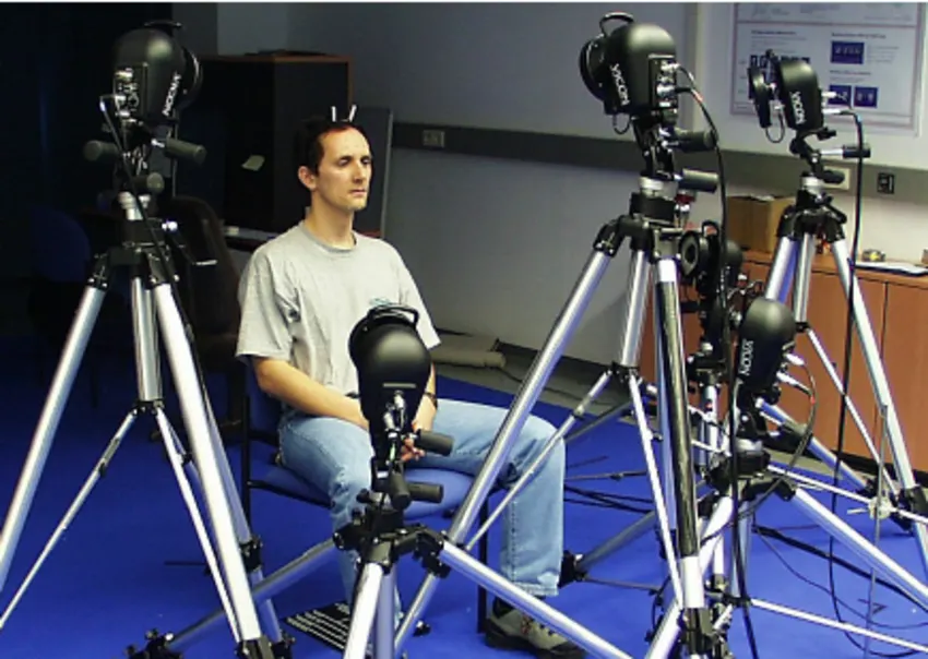 A man in a motion capture studio surrounded by multiple cameras used to record human movement data for AI and animation