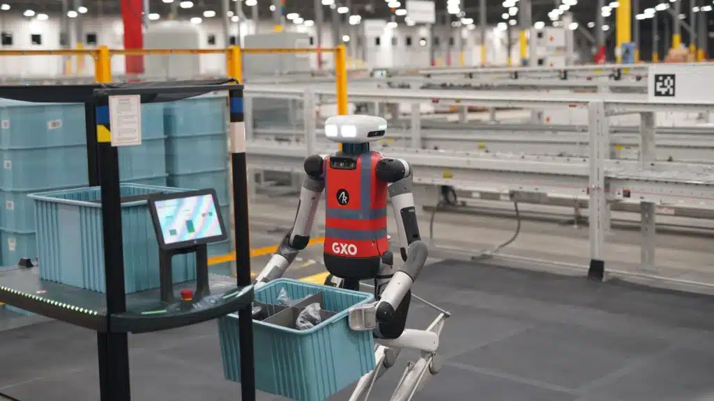 Apptronik Apollo humanoid robot carrying a plastic bin in a GXO logistics warehouse