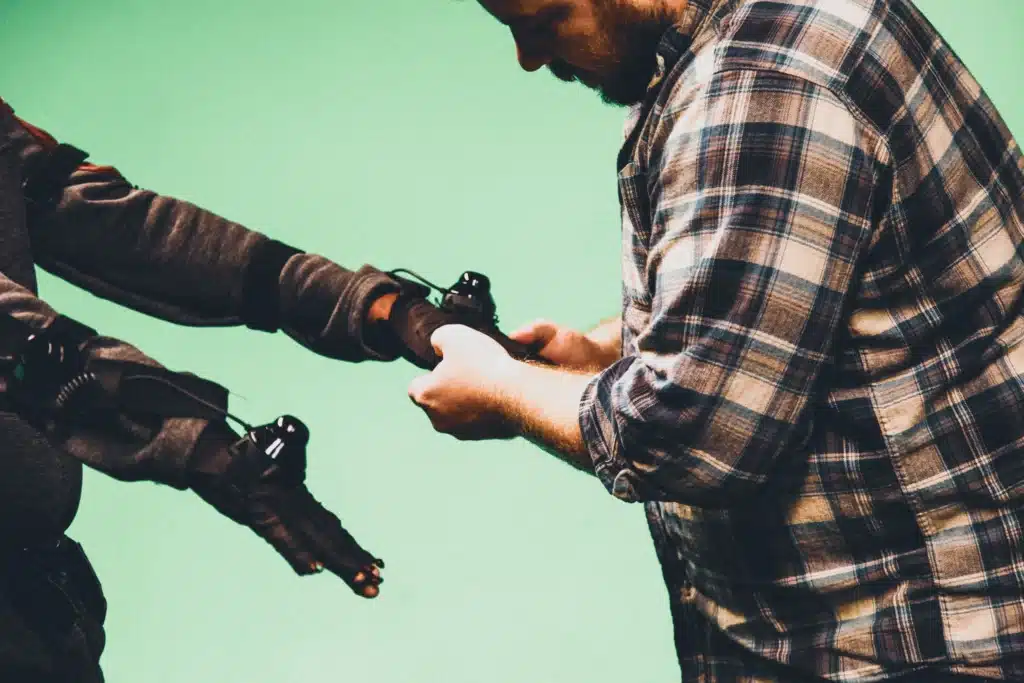 Technician adjusting wearable haptic tracking sensors on a performer's glove against a green screen