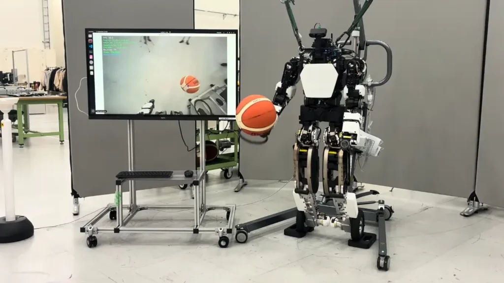 A humanoid robot learns to dribble a basketball next to a monitor showing computer vision tracking data