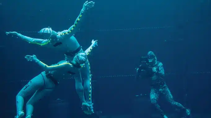 Stunt actors wearing tracking suits underwater being filmed by a camera operator for VFX production