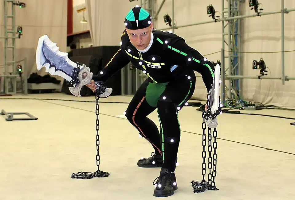 Actor in a reflective MoCap suit posing with prop swords on chains for video game animation tracking