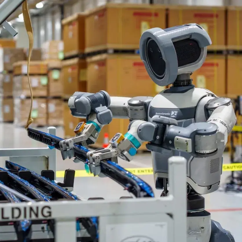 Boston Dynamics electric Atlas humanoid robot manipulating a part in a logistics warehouse