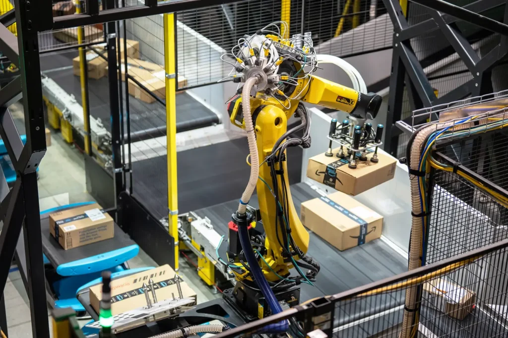 Yellow robotic arm with suction cups lifting cardboard boxes on a warehouse conveyor line