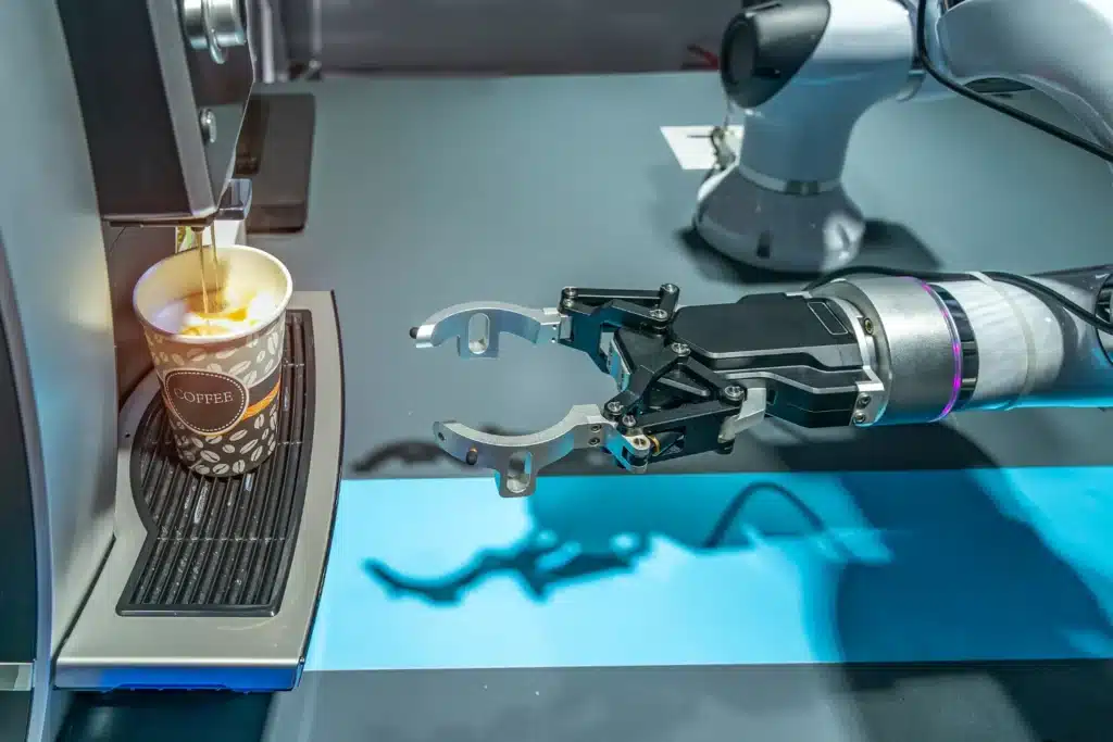 Robotic gripper arm positioned next to an automatic coffee machine pouring espresso into a cup