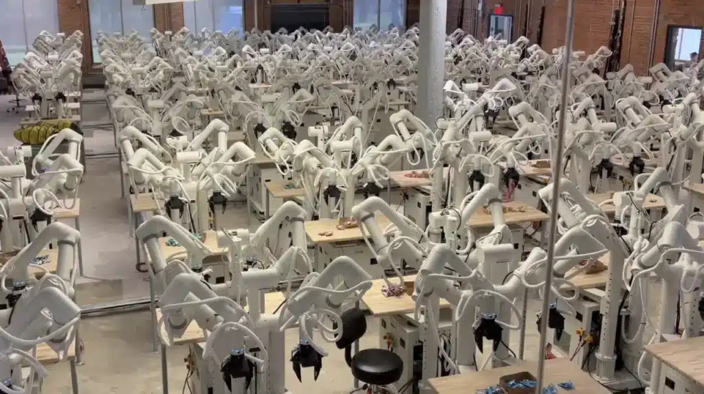A large facility containing dozens of white collaborative robotic arms set up for automated data gathering