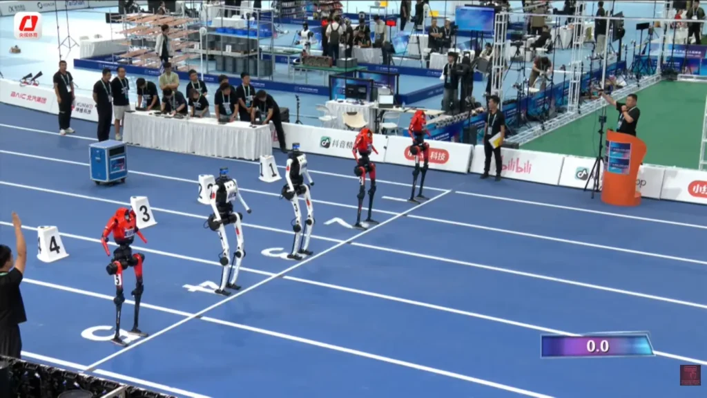 Bipedal humanoid robots lined up at starting blocks on a blue running track for an automated sprint race