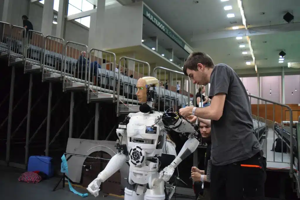 An engineer adjustments and wiring a 3D-printed humanoid robot at a robotics competition in an arena