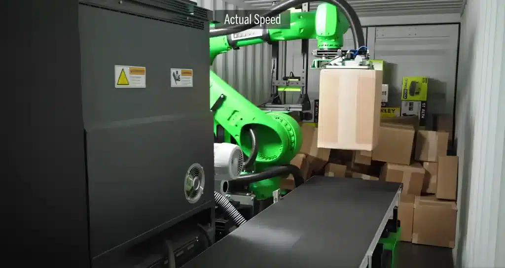 Green automated robotic arm unloading cardboard boxes from a shipping container onto a conveyor belt